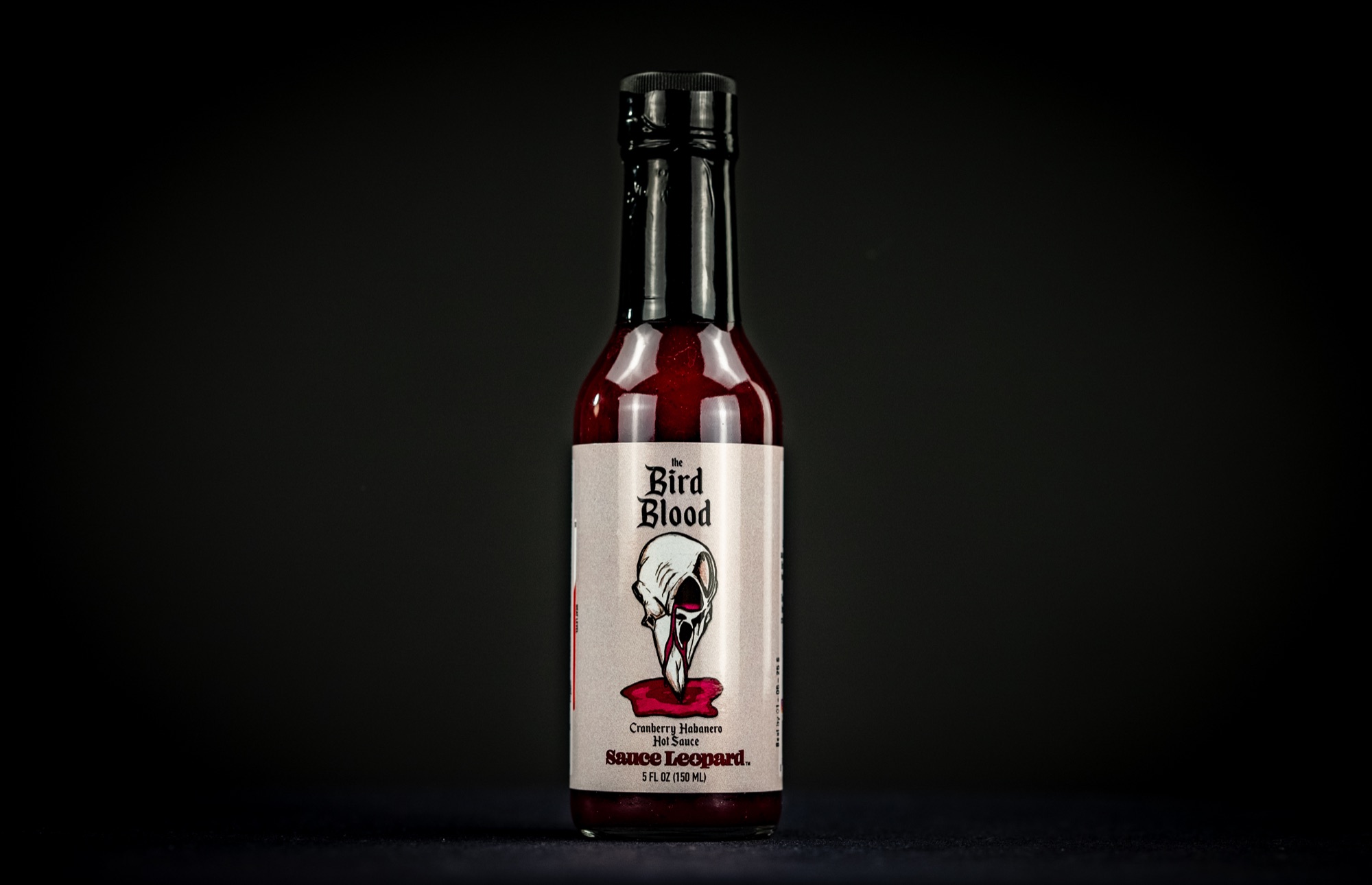 Bird Blood sauce bottle photographed outdoors with fruit and flowers